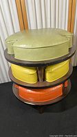 Three-tier stack of footstools: green top, yellow middle, orange bottom on dark wood bases.
