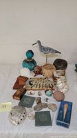 Photo showing full assortment of artisan wood craft items, painted gourd, carved bird sculpture, basket, shells, minerals, and the hand-painted egg, arranged on a white cloth surface.