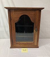 Front view of vintage wooden cabinet with arched beveled glass door and key lock