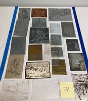 Top-down full view of all 22 etching plates arranged on white surface bordered with blue tape, showing the variety in size, shape, and material with a yellow sticky note labeled '31'