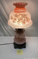 Full view of the pink frosted glass parlor lamp with floral paintings and metal base