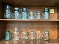 Full shelf of 12 assorted vintage glass mason jars of varying sizes and brands displayed on wood shelf