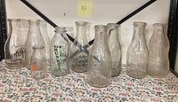 View of all 9 vintage milk bottles with various dairy branding on a floral cloth surface.