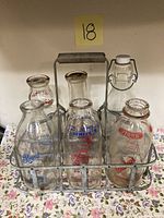 Front view of six vintage milk bottles in metal rack showing all with printed creamery logos.