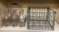 Six clear glass vintage milk bottles in metal rack, along with metal crate.