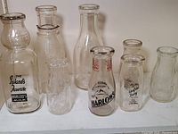Full assortment of eight vintage glass milk bottles of various sizes and embossing, some branded with Harlow's and Glensfield Dairy.