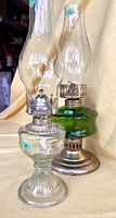 Photo showing two vintage oil lamps side by side, clear glass lamp marked A and green glass with brass marked B