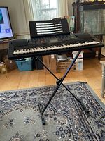 Side view showing the full keyboard on adjustable X-style stand in a room setting with hardwood floor and carpet