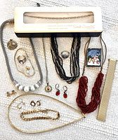 Overview of all jewelry items in lot laid out on textured fabric showing necklace, earrings, rings, bracelet, brooch, and pin
