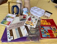 Photo of two unpainted wooden Matryoshka dolls, scrapbooking paper pads, paint trays, plastic weaving looms, and small craft accessories.