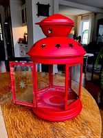 Large red farmhouse-style lantern with hinged door shown open, star cutouts on top and clear glass panels.