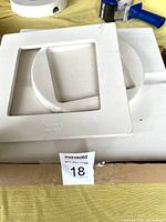 Three white ceramic glass slumping molds shown from top angles on a yellow fabric. The largest mold has a recessed square with a round inside edge, the mid-sized mold is a square with a circular recess and small holes near edge, the smallest is a flat square frame.