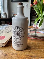 Front view of the ceramic Hudsons Bay Royal Charter whiskey bottle with cork stoppered neck and printed label on wooden surface.