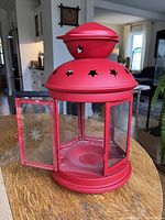 Large red metal farmhouse lantern with hinged door open showing inside candle holder. Star cutouts on the top and etched star glass panels visible.