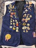 Full view of navy blue ladies vest covered in numerous colorful Lioness Club pins including embroidered lion patch on pocket.