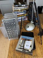 Lot displaying stack of business and self-help books, office remotes, desk organizer and mouse on wooden table.