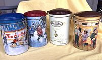 Front view of four Tim Hortons coffee tin canisters lined up showing detailed vintage 1990s themed illustrations including hockey scenes and coffee shop scenes.