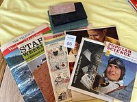 Photo of assorted vintage publications with a Popular Science magazine and other papers, books, and a bus pass on a yellow surface.