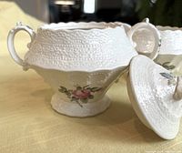 Close-up of the sugar bowl with lid removed showing embossed texture, floral design, and delicate pink rose pattern.