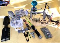 Wide view showing assortment including AT-AT Walker, Snowspeeder, pilot figure, playset with crane, green lightsaber, small toys, and character cards.