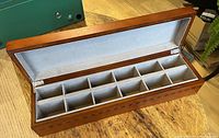 Open wooden tea chest showing 12 compartments lined with light fabric and the polished wood with diamond inlay.