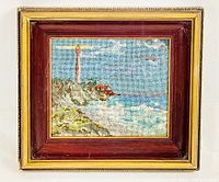 Full view of the framed miniature needlepoint embroidery showing the lighthouse, rocky coastline, ocean, and sky.