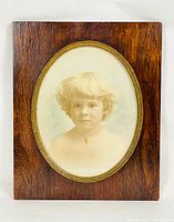 Full view of the framed antique photographic portrait showing child with blond hair, oval mat with gold trim, and wooden frame.