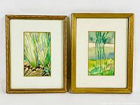 Two small framed watercolour paintings side by side, showing the natural theme with grass and landscape colors, gold-tone frames, matting and glass.