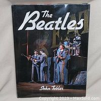 Front cover of the hardcover book showing The Beatles performing on stage with their instruments and the author's name 'John Tobler'.
