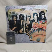 Front cover of The Traveling Wilburys Volume 1 vinyl record with a black cassette tape beside it