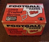 Photo of original 1989 Topps Traded Series football card box showing orange and beige color scheme, Topps and NFL logos, with some wear on the box edges.