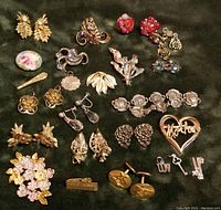 Top-down view of assorted costume jewelry pieces including clip-on earrings, pins, and cufflinks laid on green fabric
