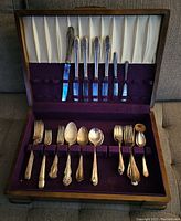 Full case open showing 18 pieces of vintage silver plated cutlery with decorative handles inside purple fabric-lined slots.
