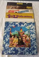 Photo showing six vintage vinyl albums stacked, including Elvis and The Monkees albums on top, colorful Jimi Hendrix Experience and others below.