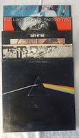 Five vintage vinyl albums stacked showing partial covers including Pink Floyd, Beatles, and Rolling Stones albums.