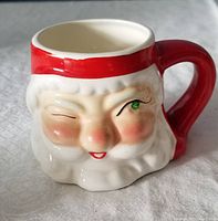 Close-up image showing the front face of the Santa mug with a winking eye, red hat rim, and red handle.