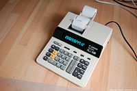 Canon MP25D printing adding machine showing digital display, keypad with numeric and function keys, and paper roll printing output.
