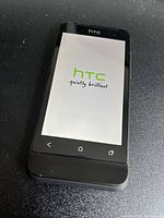 Front view of black HTC One smartphone displaying HTC boot screen logo, situated on a black surface.