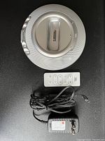 Photo showing JBL On Stage Micro V2 iPod speaker dock, white remote control, and black power adapter with cable, arranged on a black surface.