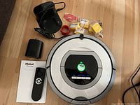 Overview of Roomba vacuum with charging station, battery pack, remote, manual, IR fence wires and cleaning accessories laid out on floor