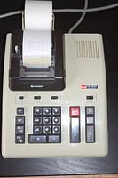 Sharp Elsi-Mate EL-1052 adding machine showing keyboard, function keys, and paper roll with printed calculations.