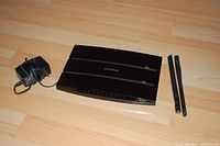 TP-Link WDR-3600 router with two antennas and power adapter shown from top side on wooden floor.