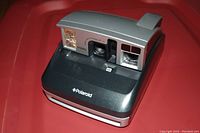 Front view of the silver and black Polaroid One600 instant camera showing lens, flash, and body condition.
