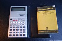 Vintage Russian Electronica MK-51 scientific pocket calculator with protective cover and manual on dark surface.
