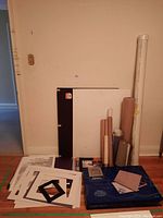 Overall view showing the entire lot with foam boards, rolled paper, portfolios, mats, and other supplies grouped together on floor against wall.