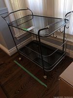 Front view of bar cart showing chrome frame, three glass shelves, curved handles and casters