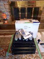 Four Bell satellite PVR units stacked on a carpet, with multiple remote controls on top and a user manual visible alongside the box.