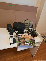 Overview photo of cameras, lenses, cases and magazines on white desk including all items in lot.