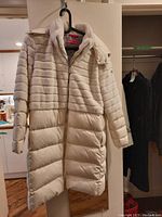 Full view of ivory puffer-and-fur coat hung on door