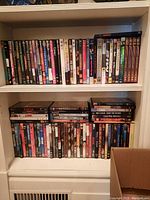 Two white shelves containing about 40 DVDs displaying a variety of movie titles including Evita and Gladiator.
